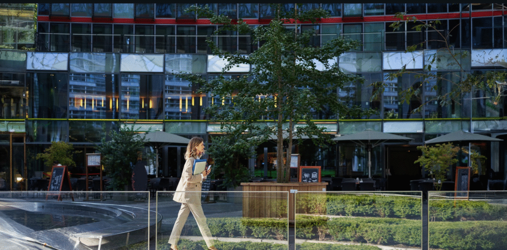 A professional woman walks past the outdoor area of a modern glass office building, representing Lets Connect’s hybrid-ready office spaces designed to support flexible work environments and set the brand apart for remote and on-site teams.